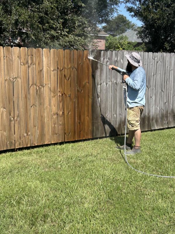 A worker washing a wood fence where cleaned boards meet weathered boards